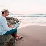 4-stelling online verdienen monat Mann mit Hut am Strand mit Laptop in die Ferne schauend make 4-figures online offline experts online income per month man sitting on beach looking to the horizon